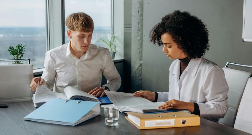 Colleagues in White Long Sleeve Shirts Sitting and Reading a report